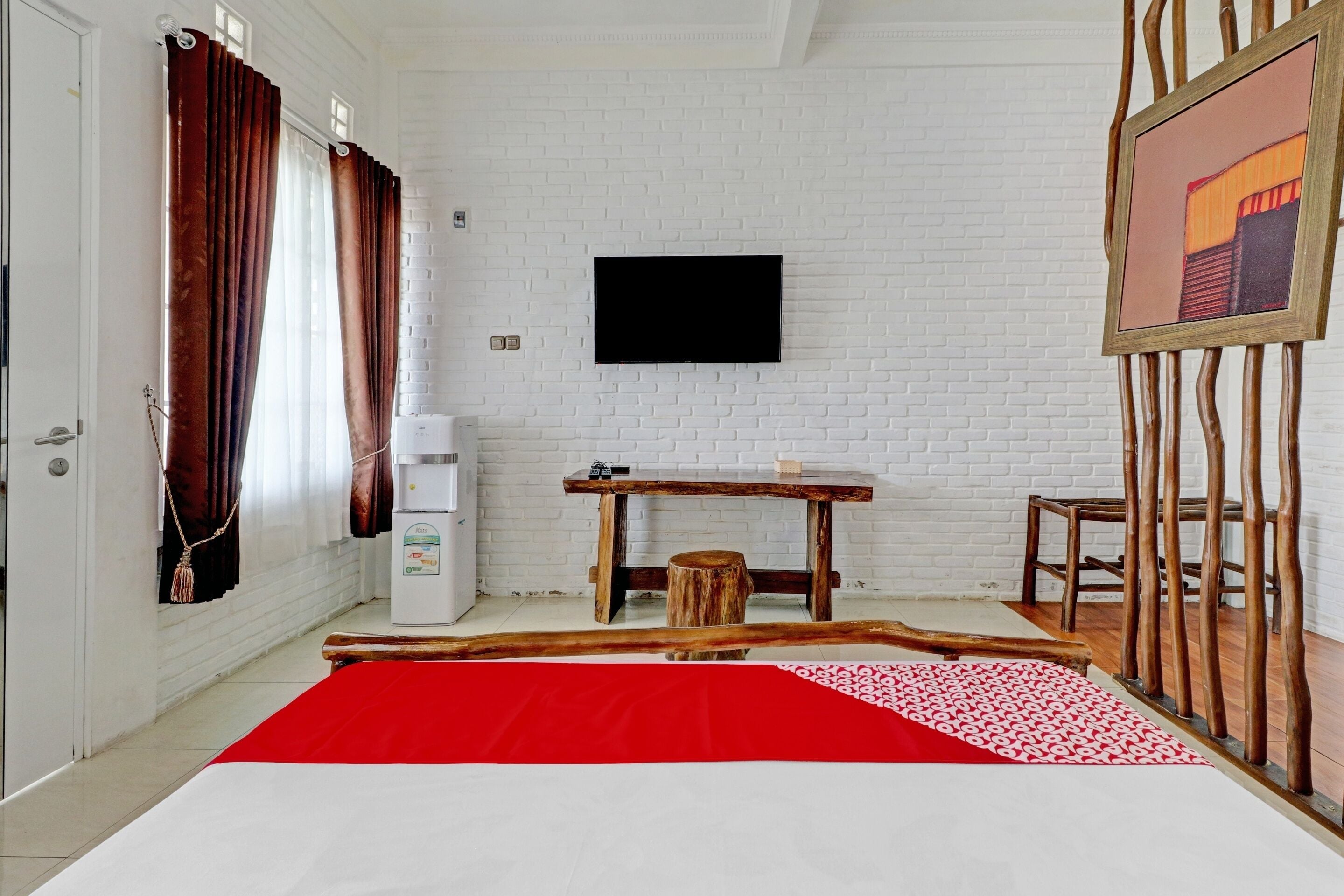 A hotel room with a bed, a desk, a chair, a television, and a white brick wall.