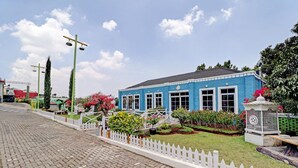 Un edificio azul con cerca blanca de piquete, un camino pavimentado y un jardín cuidado con diversas plantas y flores.