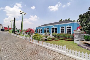 A blue building with a white picket fence, a paved walkway, and a well-maintained garden with various plants and flowers.