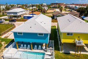 Two homes with pitched roofs and front porches sit in a coastal area, offering a swimming pool and ocean views.