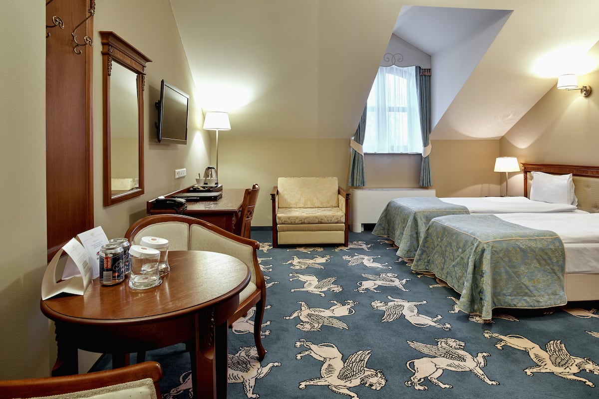 A hotel room with two beds, a desk with a chair, a small table with drinks and a menu, and a carpet with animal patterns.