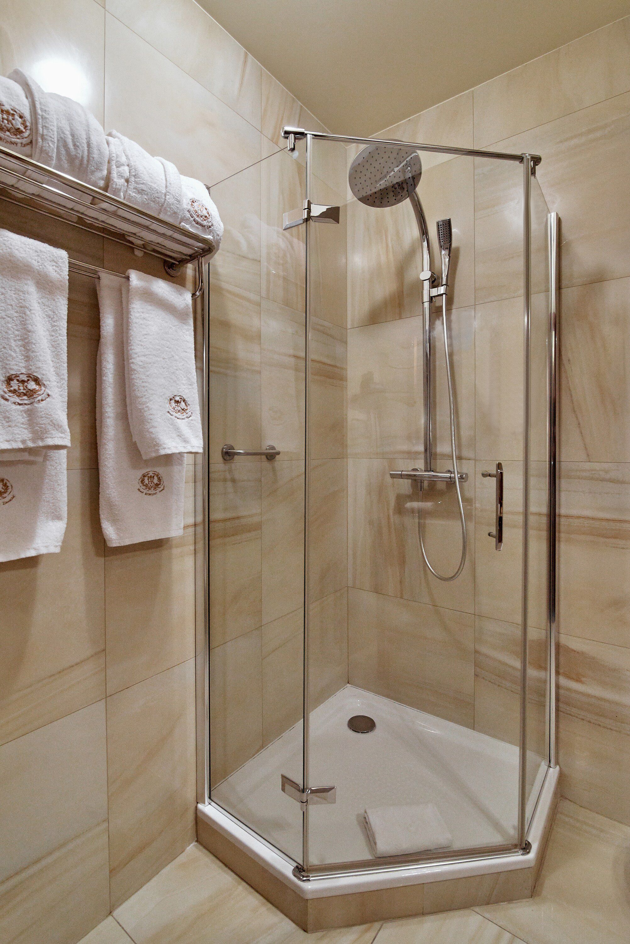 A glass-enclosed shower stall with a handheld showerhead and a wall-mounted towel rack with folded towels.