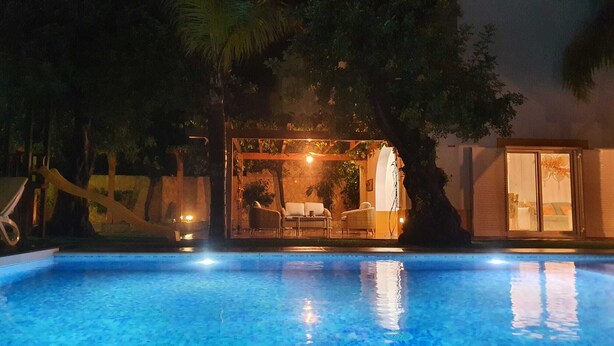 Una piscina con zona de patio, mobiliario exterior e iluminación ambiental.