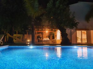 Une piscine avec un espace patio aménagé, comprenant des meubles d’extérieur et un éclairage d’ambiance.