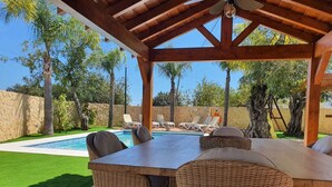 Un espacio al aire libre techado con piscina, mobiliario de mimbre y una pared de piedra.