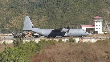 Un grand avion militaire est stationné sur une piste d’atterrissage, avec une chaîne de montagnes en arrière-plan.