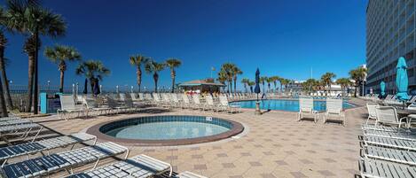 A poolside area with lounge chairs, palm trees, and a building in the background.