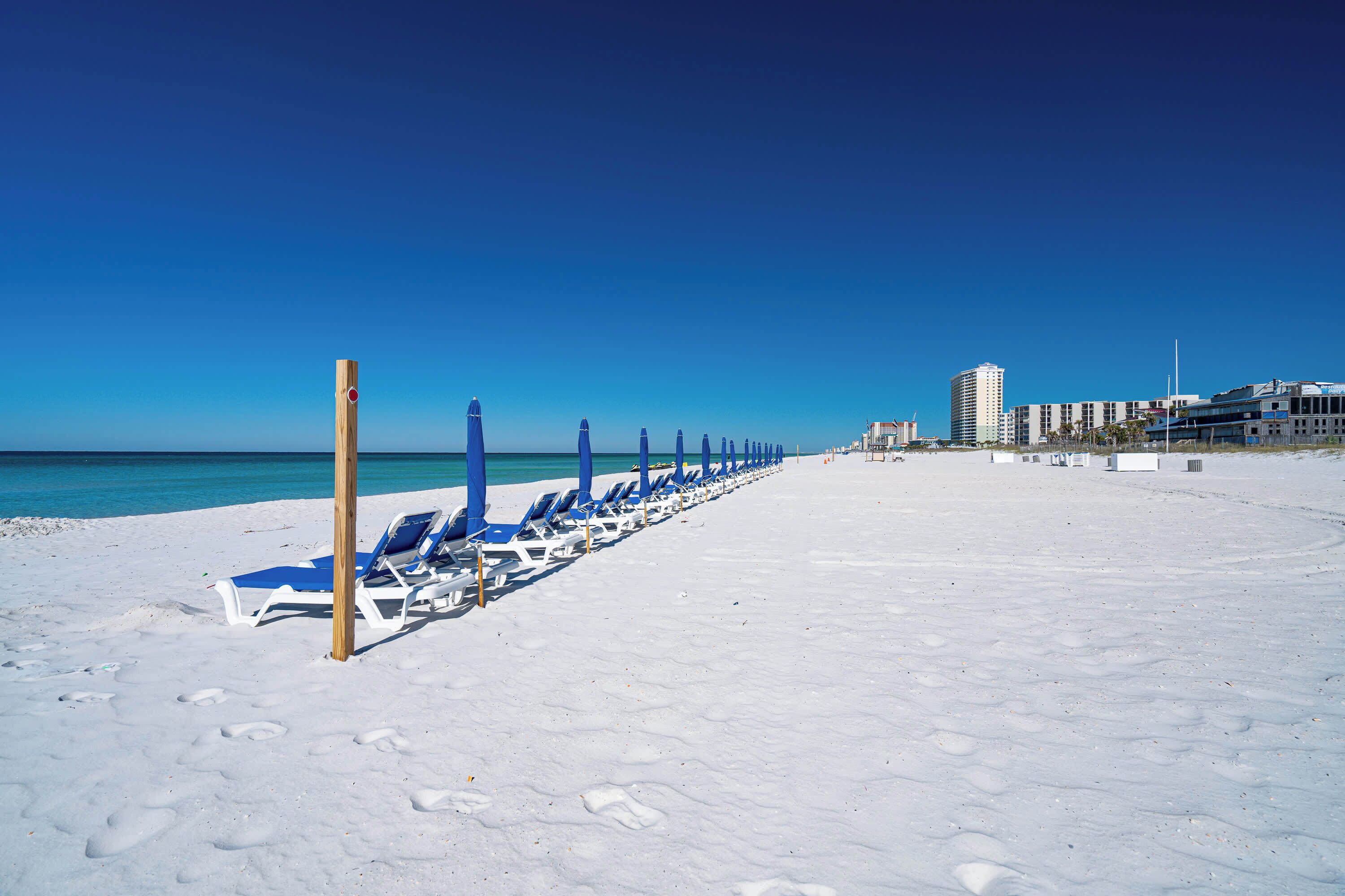 A beach with rows of blue lounge chairs and a clear blue sky.