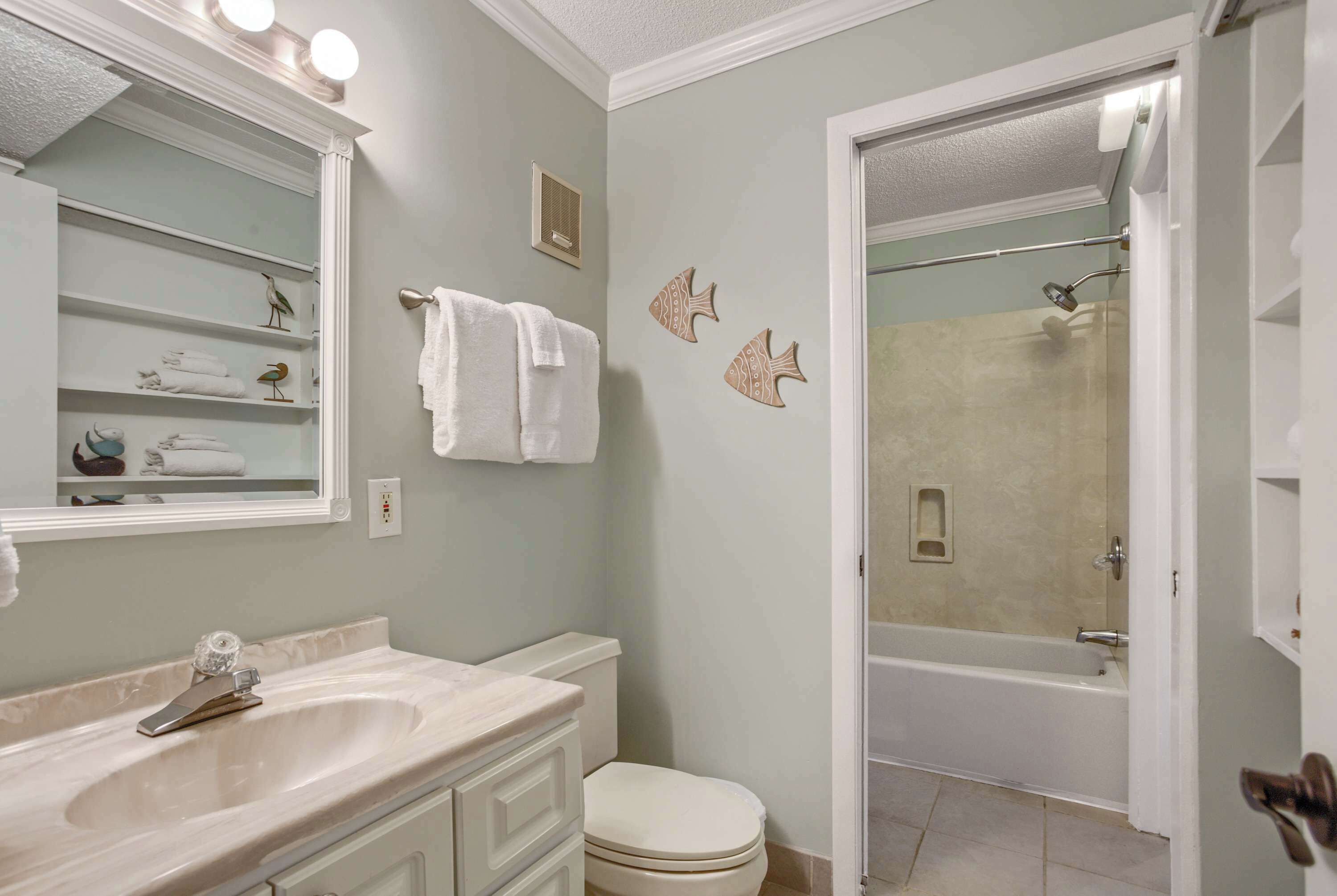 A bathroom with a sink, toilet, and shower. There are towels hanging on the wall and a mirror above the sink.