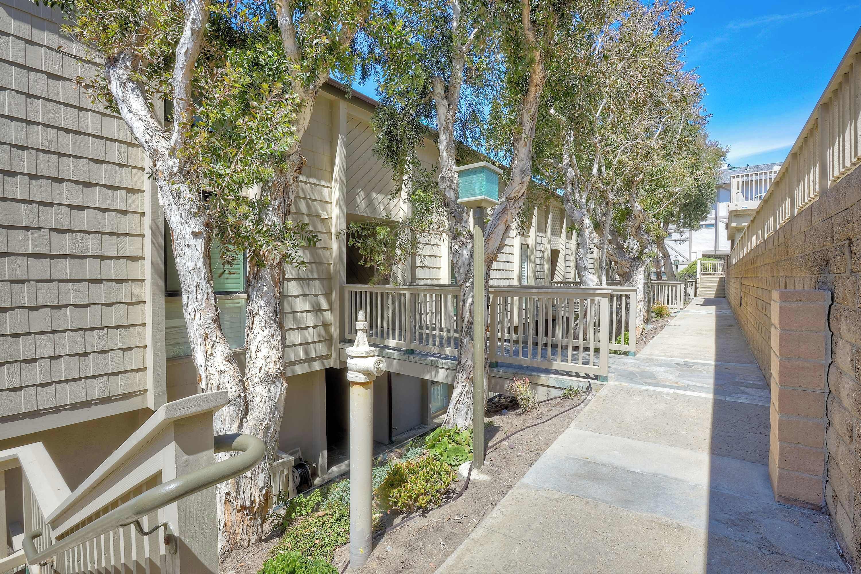 A residential building with a covered walkway, trees, and a small garden area.