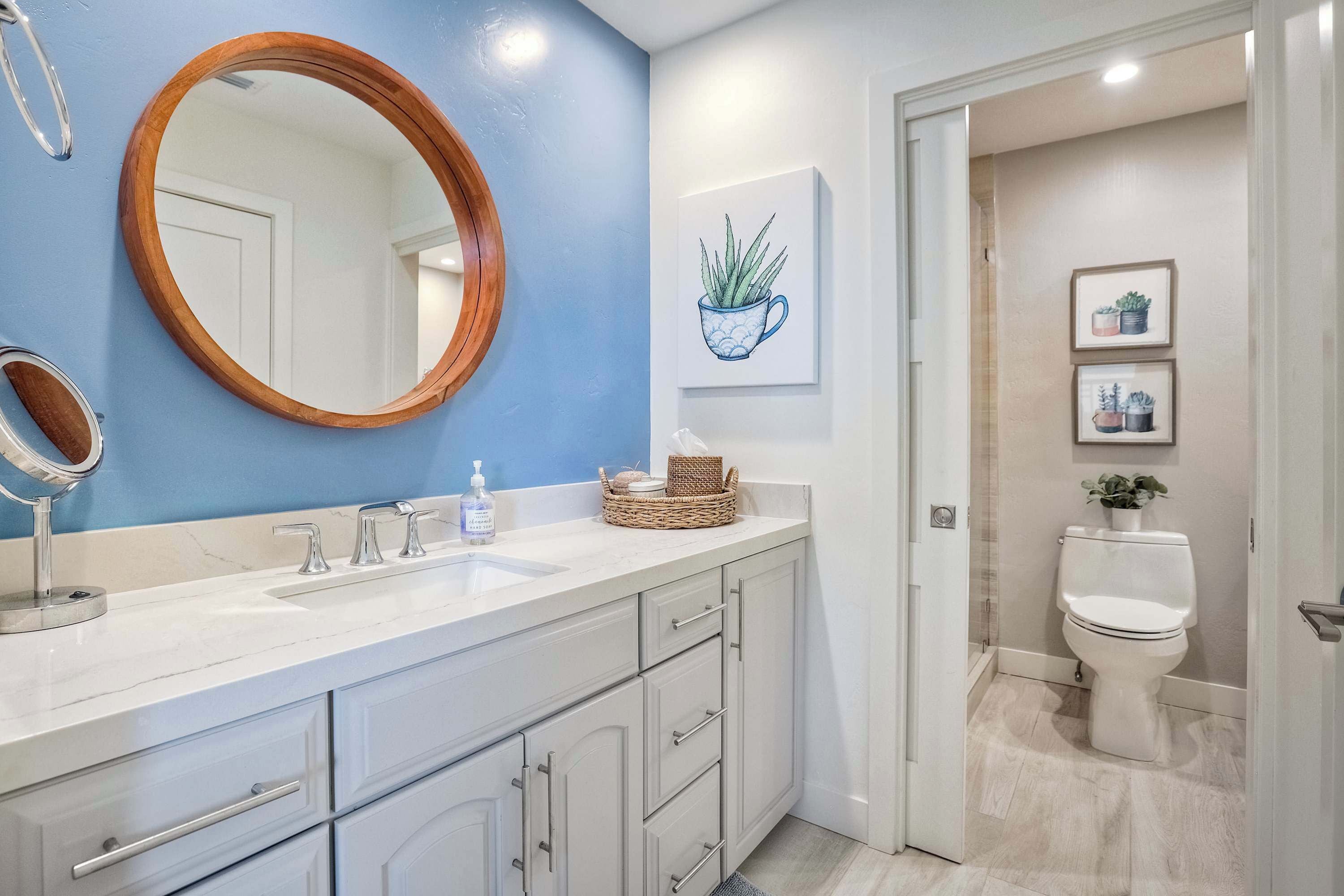 Ein Badezimmer mit weißem Waschtisch, einem spiegelnden Holzrahmen, einer blauen Akzentwand und einer Toilette mit einem Blumentopf.