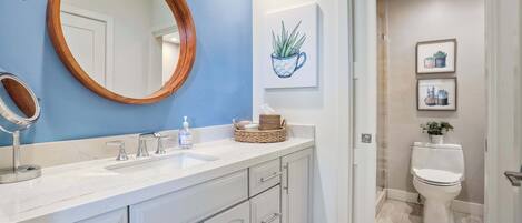 Ein Badezimmer mit weißem Waschtisch, einem spiegelnden Holzrahmen, einer blauen Akzentwand und einer Toilette mit einem Blumentopf.