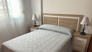 Un lit bien fait, recouvert d’une courtepointe blanche à motifs, avec deux tables de chevet dotées de lampes et une tête de lit en bois.