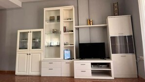Un salon avec un téléviseur, des meubles blancs et un luminaire au plafond.