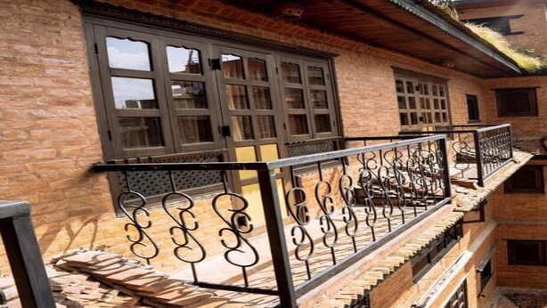 Un edificio tradicional con fachada de ladrillo, un balcón con barandillas de metal ornamentadas y ventanas grandes con múltiples divisiones.