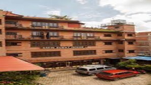 Un edificio de varios pisos con un letrero que dice “Hotel”. Hay vehículos estacionados frente al edificio, el cual tiene varios balcones.
