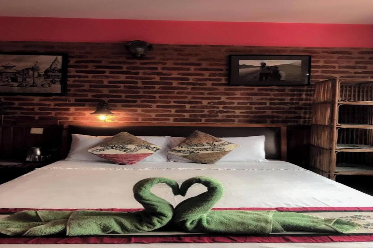 A hotel room with a brick wall, a bed with white bedding, two pillows with a design, a green towel, and a picture on the wall.