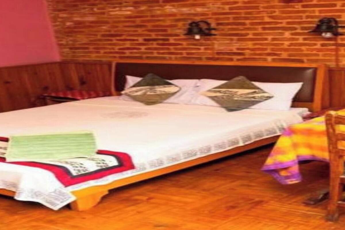 A room with a bed, a wooden table with a colorful tablecloth, and a brick wall.