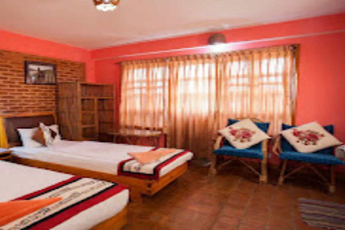 A hotel room with two beds, a brick wall, a wooden cabinet, and a window with curtains.