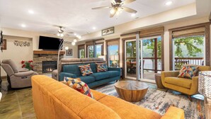 A spacious living room with a blue sofa, orange armchairs, and a ceiling fan. - That Lakefront Taneycomo House - Branson (Branson)