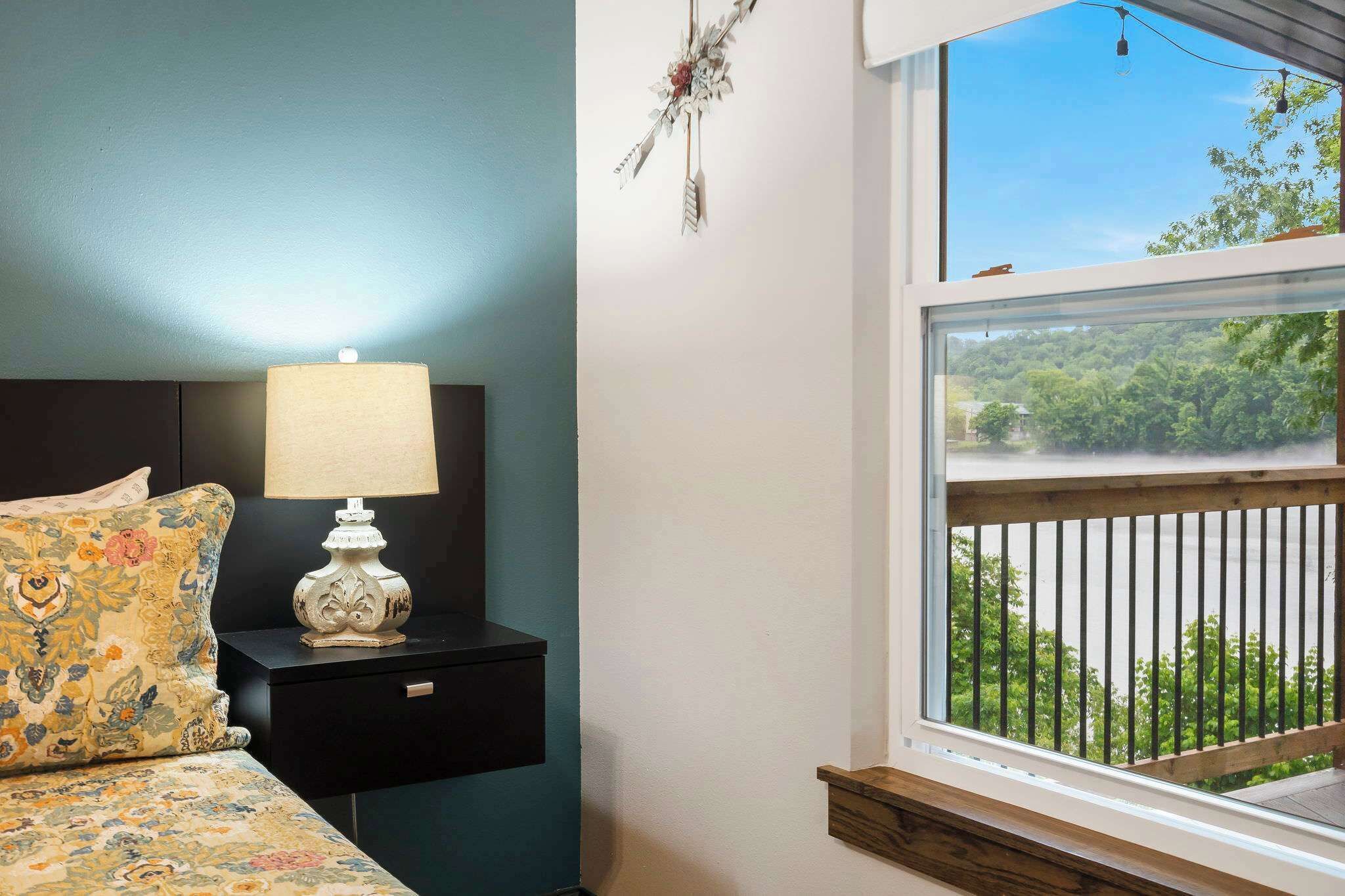 A bedroom with a bed, a nightstand, a lamp, and a window with a view of greenery.