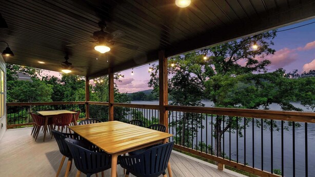 A covered outdoor deck with a wooden table and chairs, overlooking a lake with trees and a sunset sky. - That Lakefront Taneycomo House - Branson (Branson)