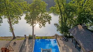 A swimming pool with a view of a lake, surrounded by trees and a small deck area with seating. - That Lakefront Taneycomo House - Branson (Branson)