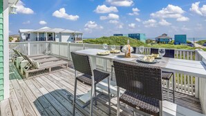 A wooden deck with outdoor furniture, a table set for dining, and a view of the ocean and buildings in the background.