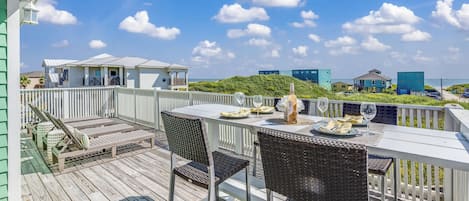 A wooden deck with outdoor furniture, a table set for dining, and a view of the ocean and buildings in the background.