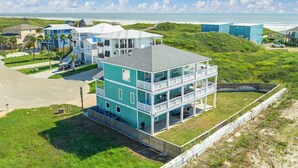 A multi-story beachfront property with a prominent balcony, a driveway, and a view of the ocean.