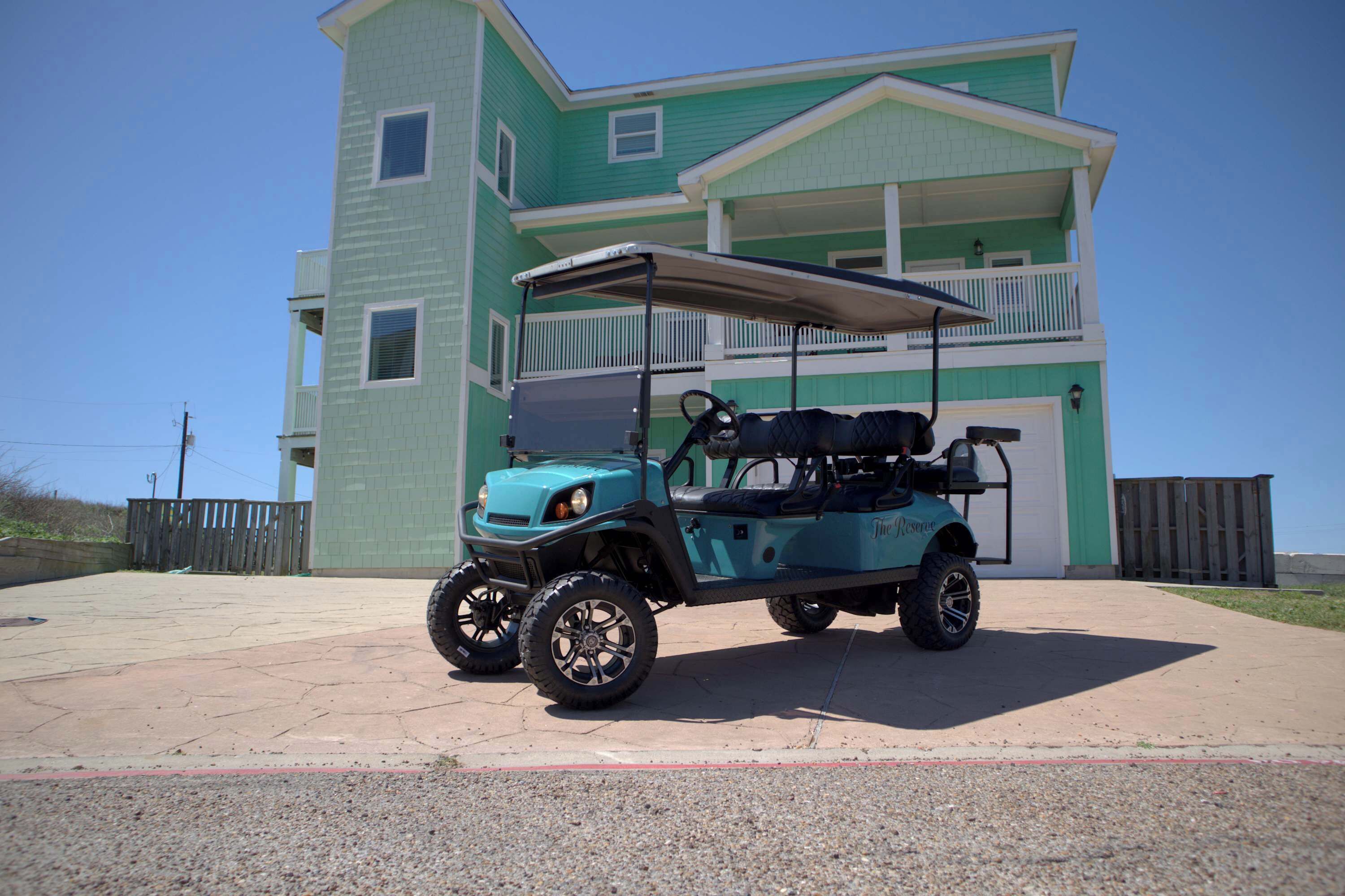 A teal golf cart parked in front of a two-story building with a balcony.