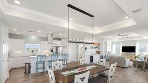 A spacious kitchen with white cabinetry, a central island, and a dining area with a wooden table and white chairs.