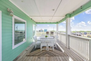 A covered porch with a table and chairs, a view of the beach, and a white railing. - Ocean Views Optional Golf Cart Sleeps 14 (Port Aransas)