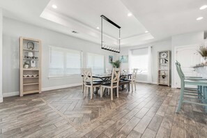 A spacious dining area with a wooden herringbone floor, a central dining table with chairs, and a modern pendant light. - Ocean Views Optional Golf Cart Sleeps 14 (Port Aransas)