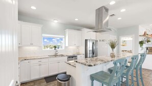 A modern kitchen with white cabinets, a stainless steel refrigerator, and a marble countertop.