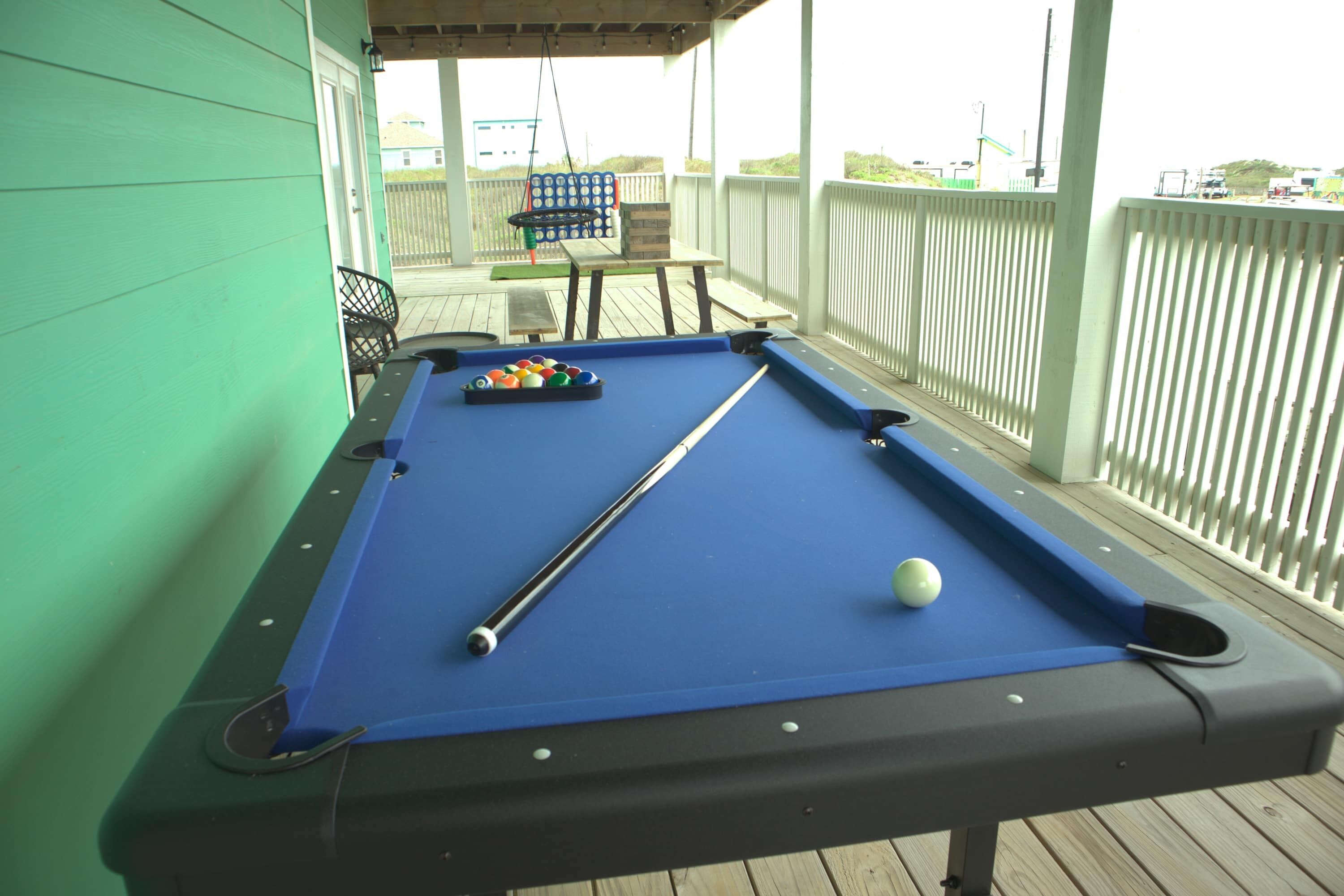 A pool table on a wooden deck with a white fence in the background.