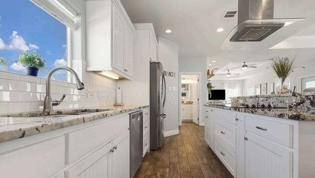 A modern kitchen with white cabinetry, a stainless steel refrigerator, and a granite countertop.