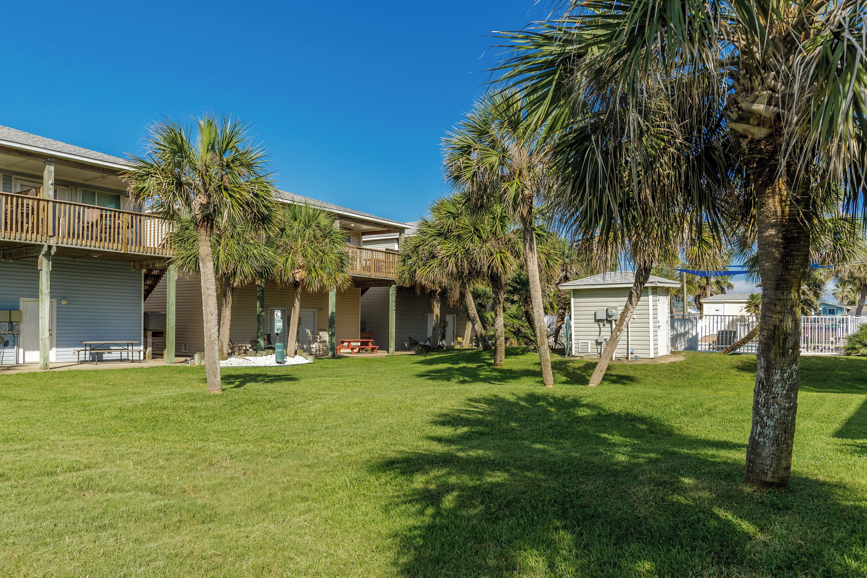 A courtyard with palm trees, a pool, and a building with a balcony.