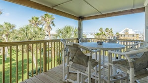 A wooden deck with a round table and chairs, overlooking a well-maintained lawn and palm trees. - The Oasis Pet Friendly Optional Golf Cart (Port Aransas)