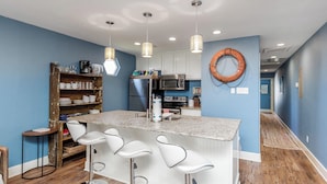 A kitchen with a bar area, white bar stools, a wooden shelf, and a life ring on the wall. - The Oasis Pet Friendly Optional Golf Cart (Port Aransas)