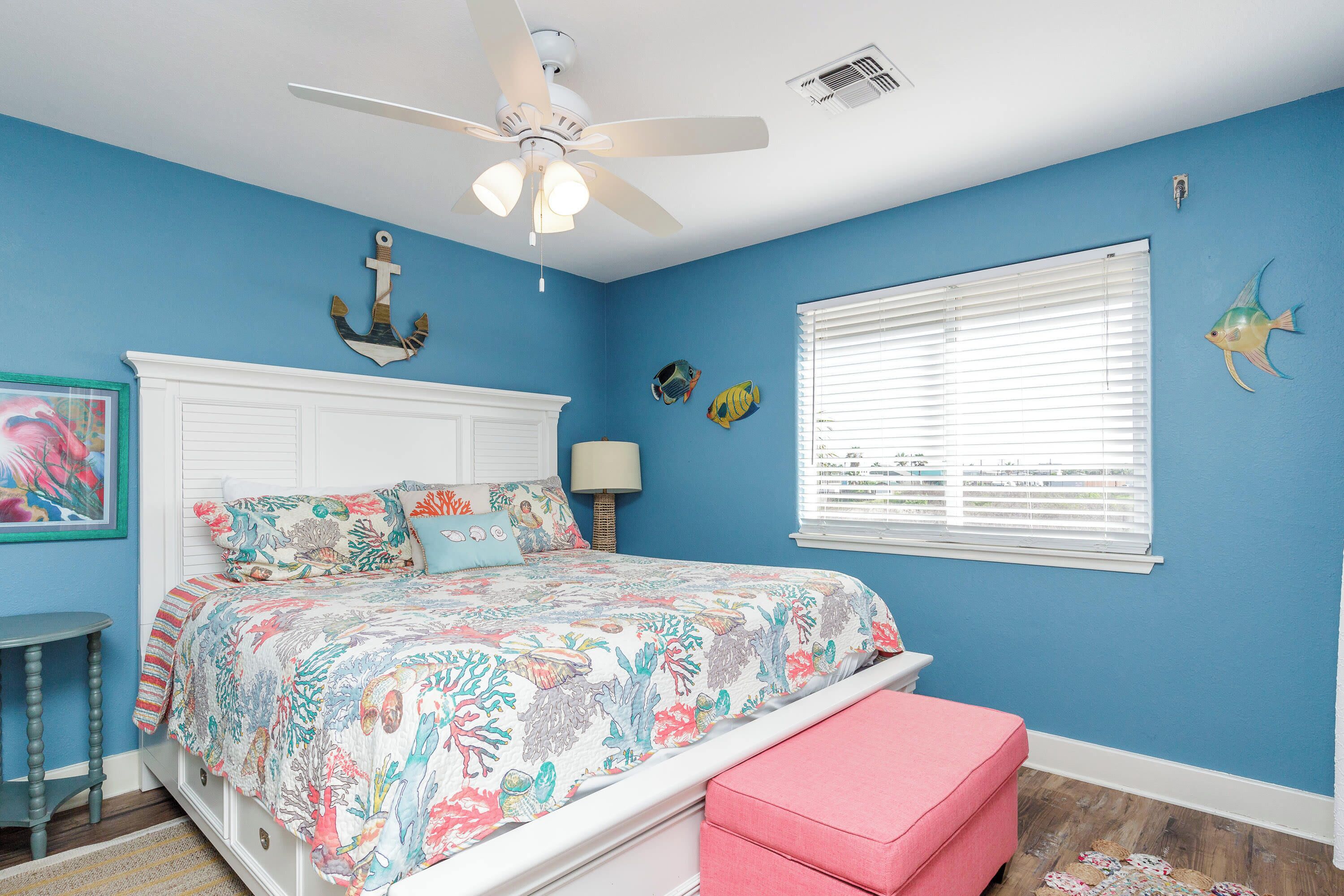 Une chambre à coucher avec un lit, un ventilateur de plafond, une fenêtre avec des stores et des poissons décoratifs sur le mur.
