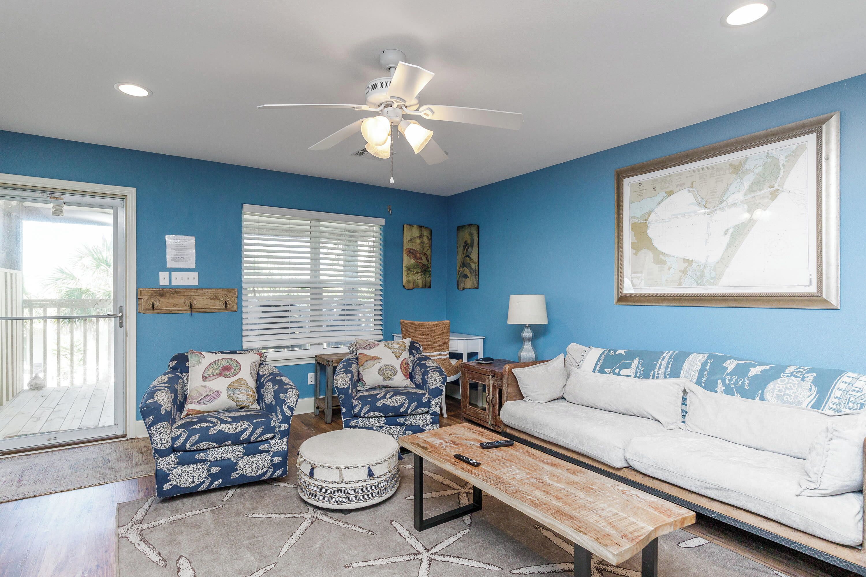 A living room with a blue wall, a white sofa, patterned armchairs, a wooden coffee table, and a ceiling fan.