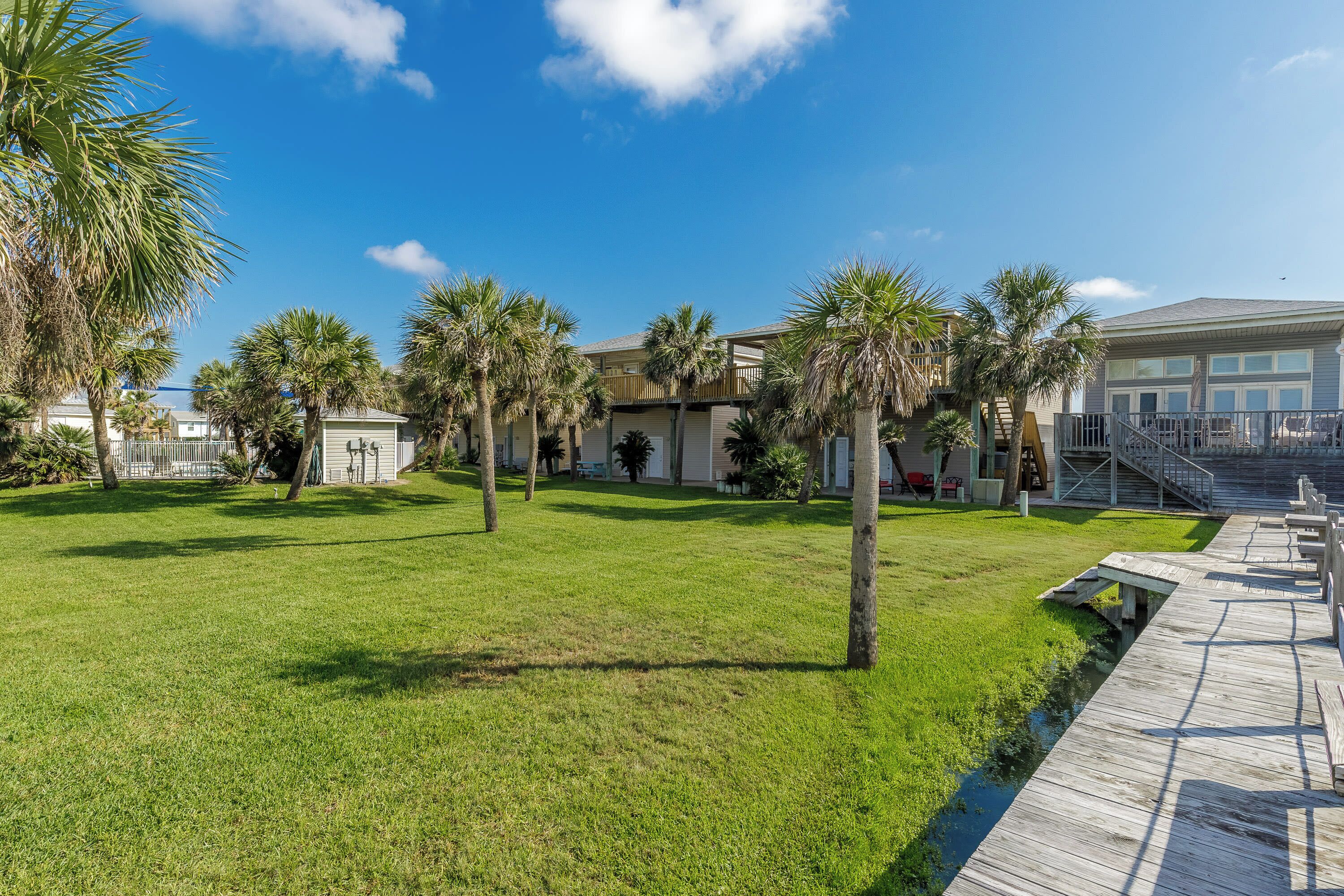 A well-maintained grassy area with palm trees, a wooden boardwalk, and a building with a balcony.