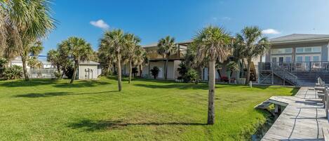 A well-maintained grassy area with palm trees, a wooden boardwalk, and a building with a balcony.