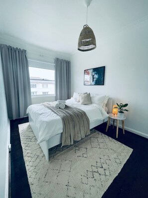 Relax in this serene bedroom with a large bed, woven pendant light, and a potted plant.
