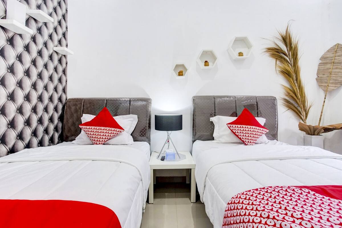 Habitación de hotel con dos camas, cabecero capitonado, mesitas de noche con lámparas y estanterías decorativas en la pared.