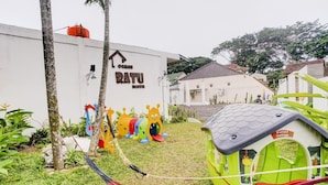 A hostel named "Oman Ratu Hostel" with a white exterior, a water tank on the roof, and a play area with colorful structures. - OYO 90124 Oemah Ratu Hostel Syariah (Bandar Lampung)