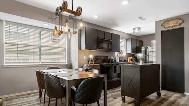 Une cuisine moderne avec des meubles de couleur sombre, un îlot central et des luminaires suspendus.
