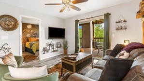 Un salon comprenant un canapé, une table basse, un téléviseur et un ventilateur de plafond. Une porte coulissante donne accès à un balcon.