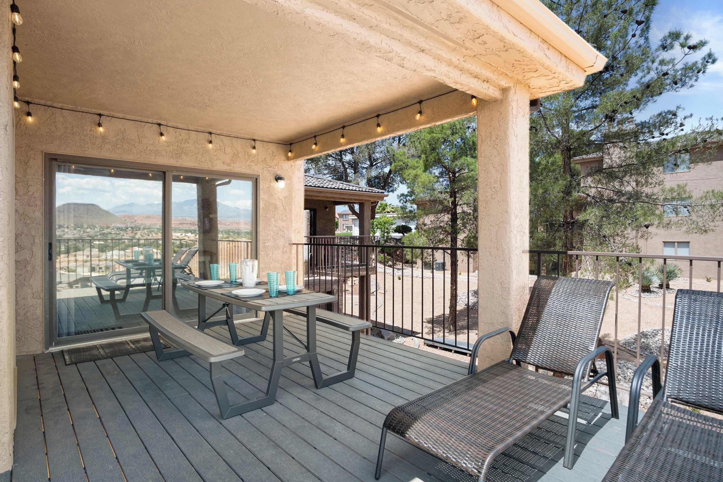 Un patio techado al aire libre con una mesa y sillas, luces colgantes y vistas al paisaje.